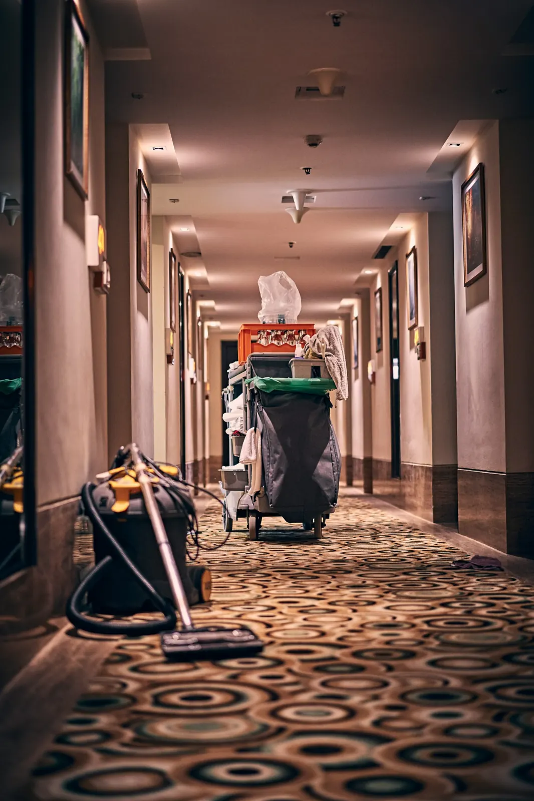 Carro de aseo y aspiradora en el pasillo alfombrado de un hotel