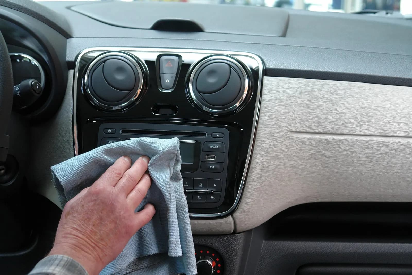 Mano limpiando el tablero de un auto con un paño de microfibra